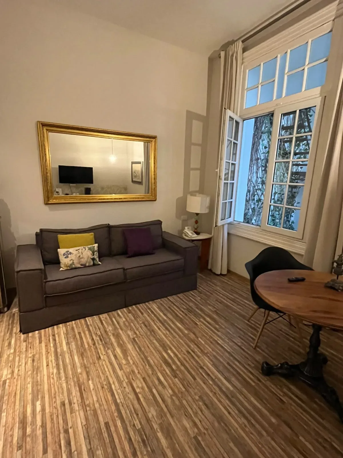 Habitación de Casa Goliana con sala, sofá, espejo dorado y ventanal hacia la calle