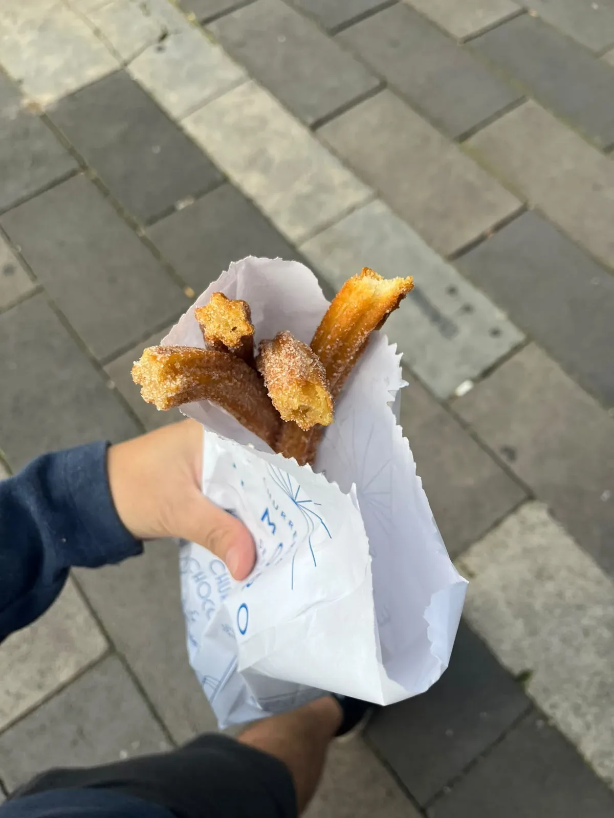 Bolsa de papel de El Moro con churros con azúcar sostenida en la banqueta