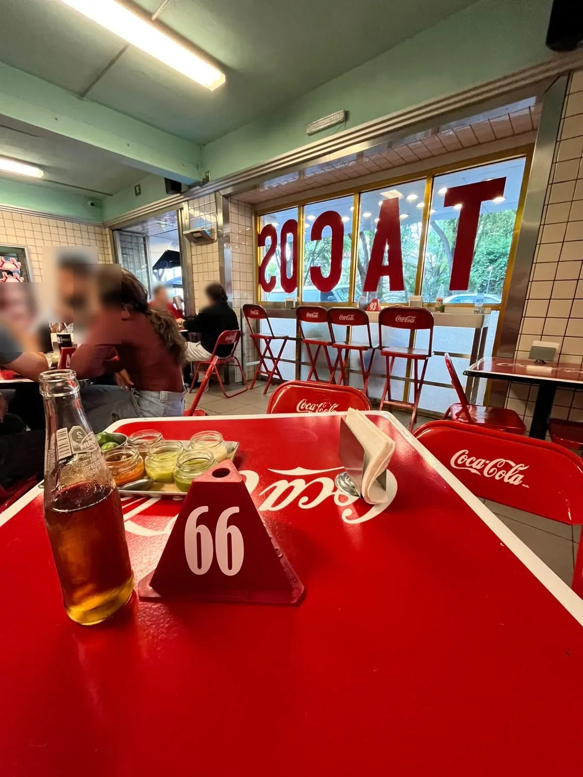 Comedor de Taquería Orinoco con mesas rojas, azulejo blanco y letras TACOS en el ventanal